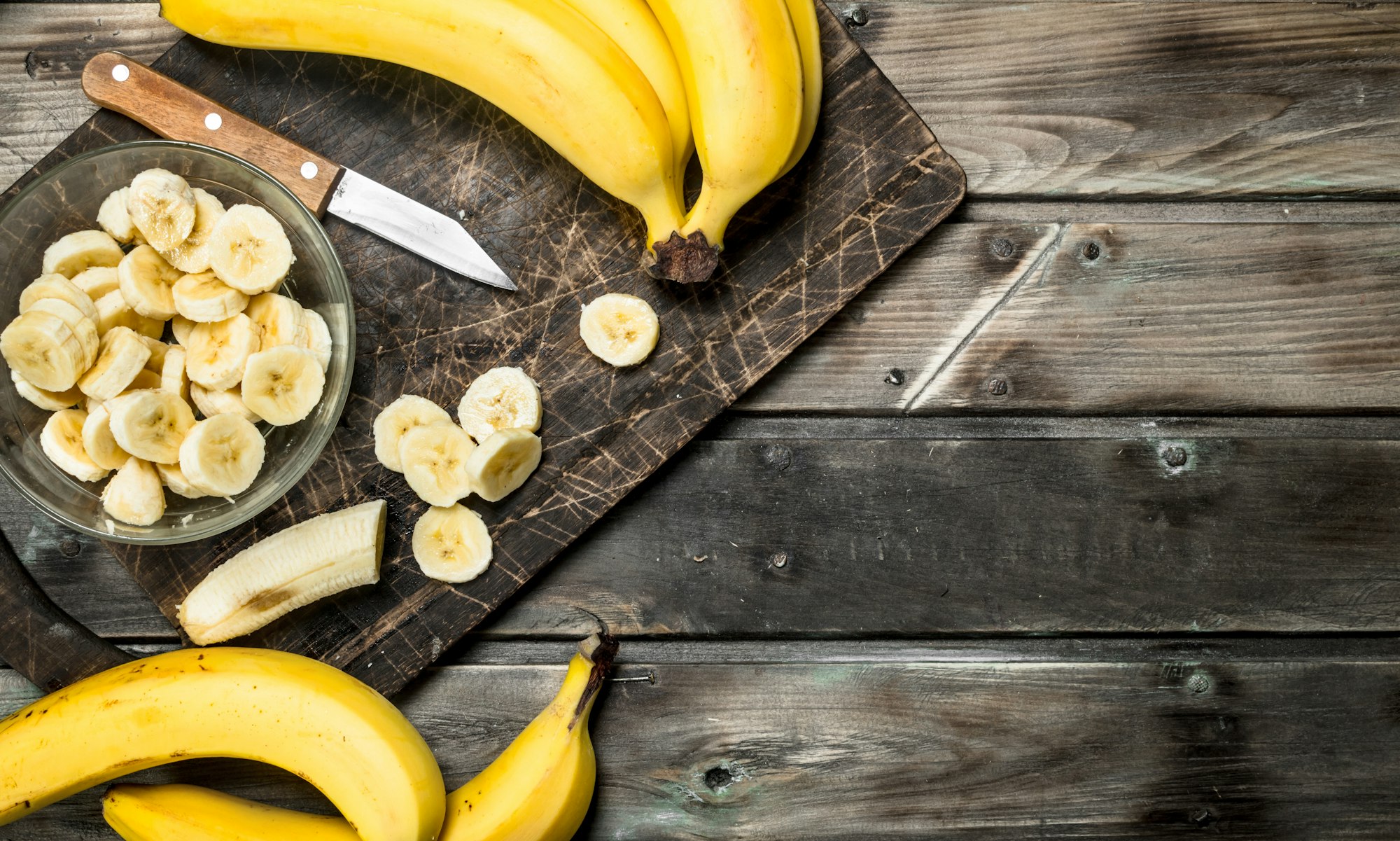 Bananas and banana slices in a plate on a black chopping Board with a knife.