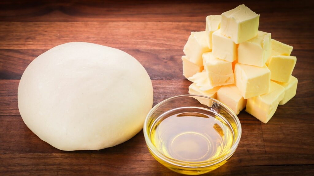 Closeup shot of dough, butter, and oil on a wooden table