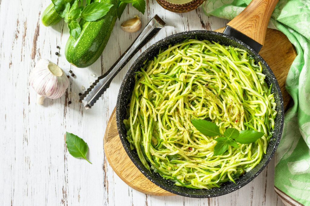 Cooked zucchini noodles with basil and garlic on a rustic wooden table.