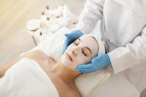 Cosmetology. Beautician doctor applying face mask to young woman in spa salon
