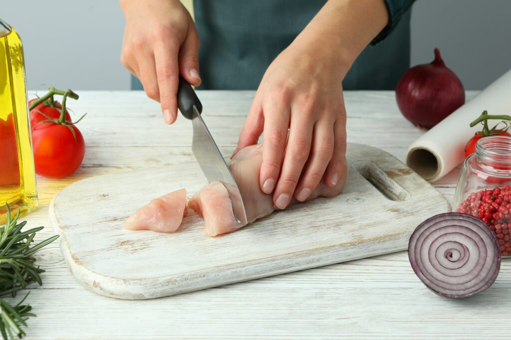 Female hands cut raw chicken fillet on wooden board