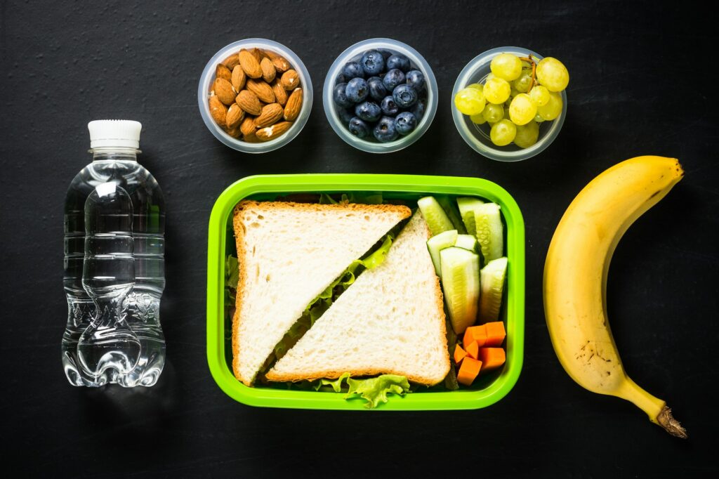Lunch box with sandwich and fruits on black