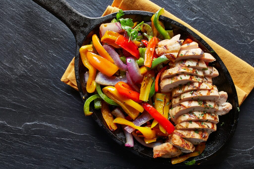 mexican grilled chicken fajitas in iron skillet shot from overhead on slate