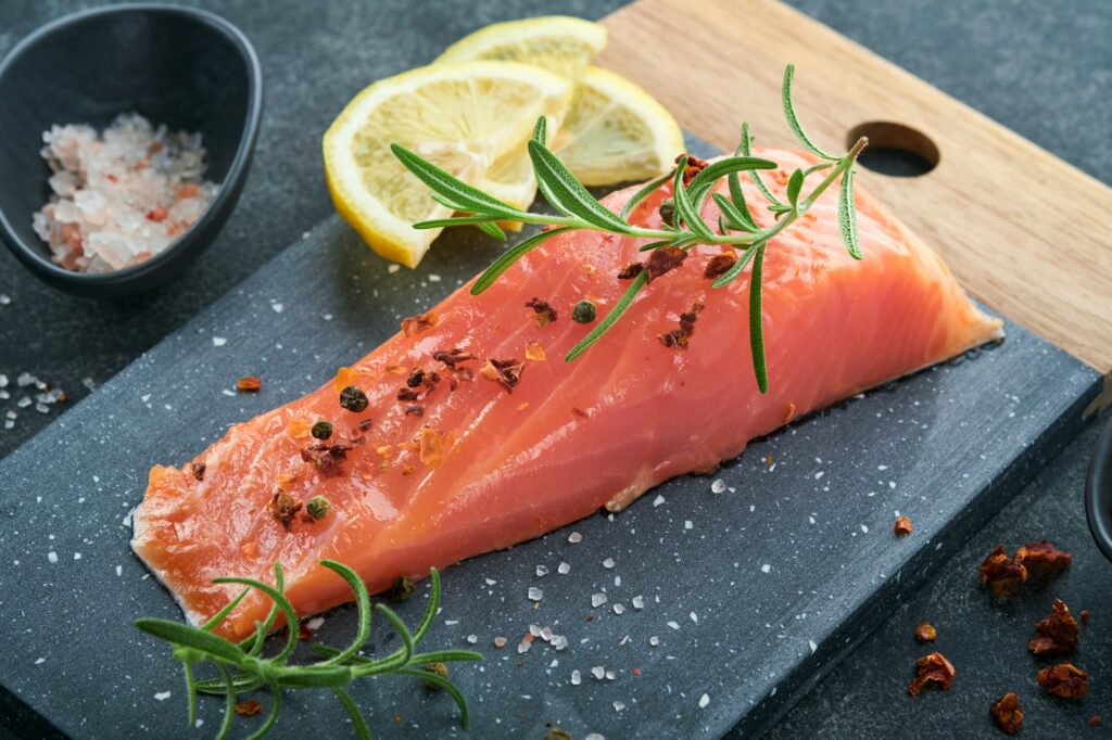 Salmon fish piece. Fresh raw salmon fish piece on marble board stand with herbs and lemon on black b