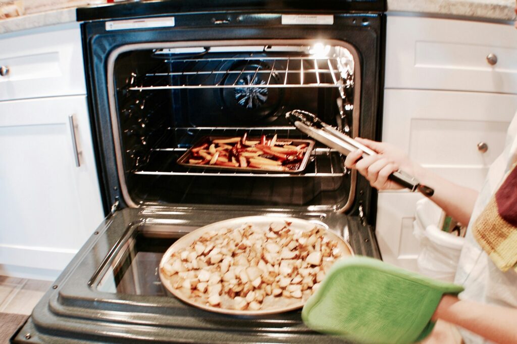 Woman taking cooked food items out of oven in kitchen